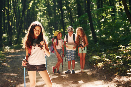 Girl standing in front of her friends. Kids strolling in the forest with travel equipmentの写真素材