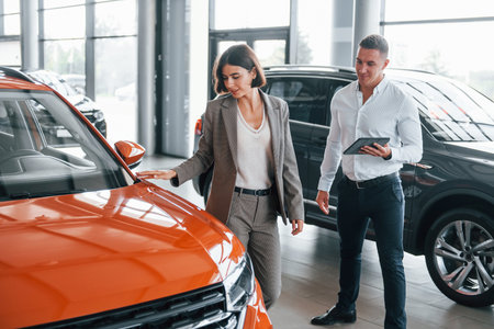 With notepad. Man in formal wear helping customer with choice of the automobileの写真素材