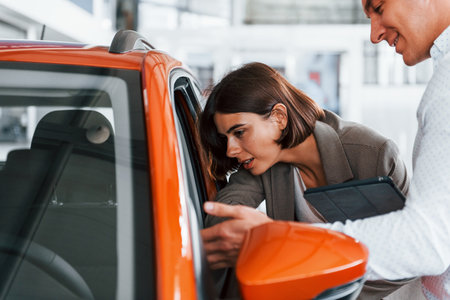 Orange colored car. Man in formal wear helping customer with choice of the automobileの写真素材