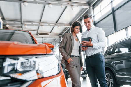 Talking with each other. Man in formal wear helping customer with choice of the automobileの写真素材