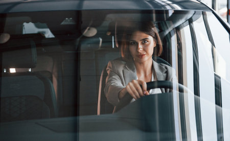 Black colored vehicle. Woman testing new car. Sitting indoors in modern automobileの写真素材