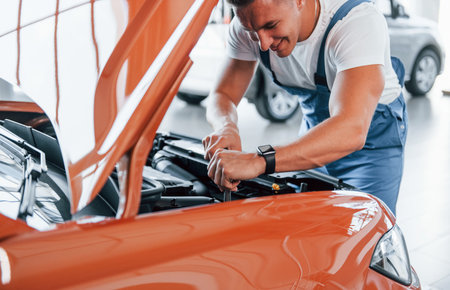 Under the hood. Man in uniform is repairing broken automobile indoorsの写真素材