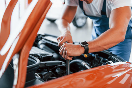 Under the hood. Man in uniform is repairing broken automobile indoorsの写真素材