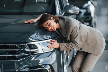 Black colored car. Woman is indoors near brand new automobile indoorsの写真素材