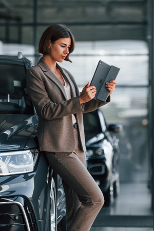 With tablet in hands. Woman is indoors near brand new automobile indoorsの写真素材