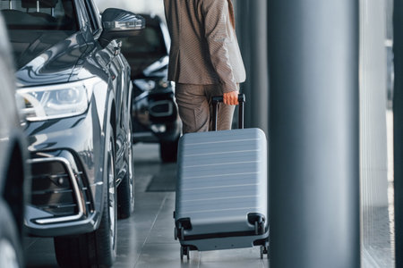 Holding luggage. Woman is indoors near brand new automobile indoorsの写真素材