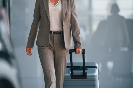 In formal clothes. Woman with luggage is standing indoors. Conception of tourismの写真素材