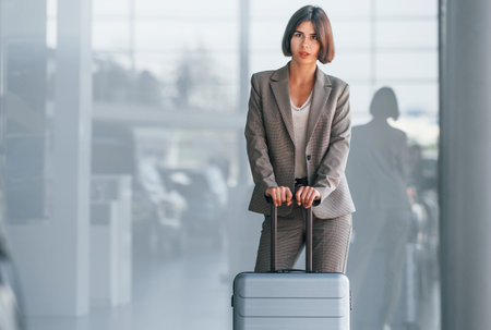 In formal clothes. Woman with luggage is standing indoors. Conception of tourismの写真素材
