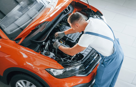 Professional service. Man in uniform is repairing broken automobile indoorsの写真素材