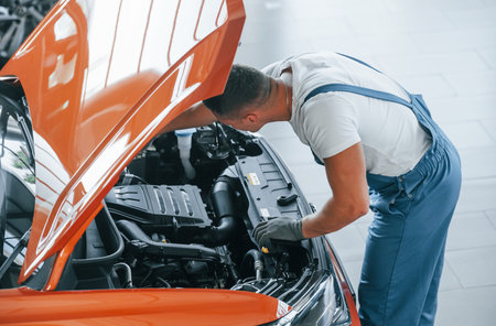 View from above. Man in uniform is repairing broken automobile indoorsの写真素材