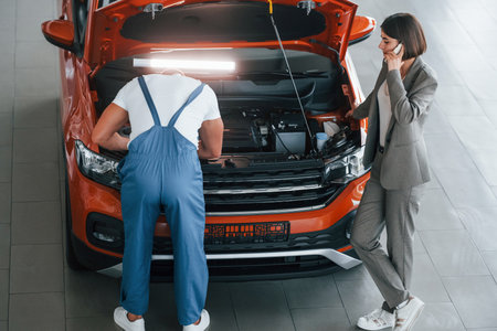 Owner standing near the man that repairing automobile indoors. Professional serviceの写真素材