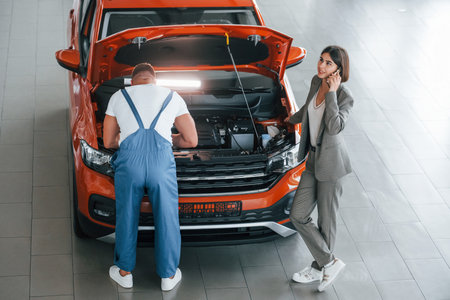 Woman in stylish clothes. Man repairing womans automobile indoors. Professional serviceの写真素材