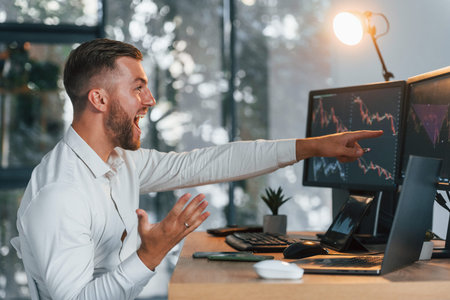 Successful young businessman in formal clothes is in office with multiple screens