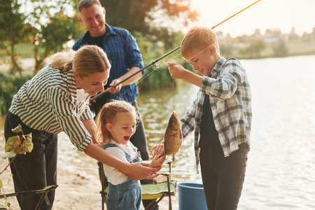 Positive emotions. Father and mother with son and daughter on fishing together outdoors at summertimeの写真素材