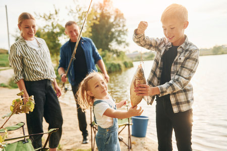 Big catch. Father and mother with son and daughter on fishing together outdoors at summertimeの写真素材