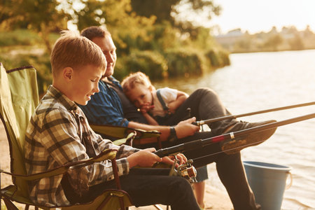 Sitting together. Father with son and daughter on fishing outdoors at summertimeの写真素材