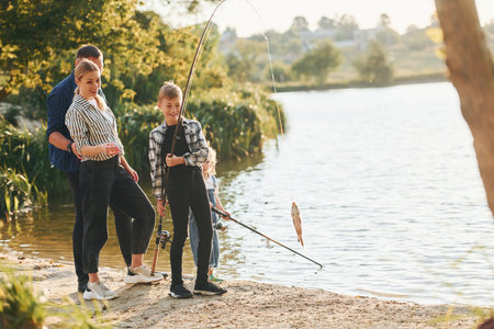 Middle sized lake. Father and mother with son and daughter on fishing together outdoors at summertimeの写真素材