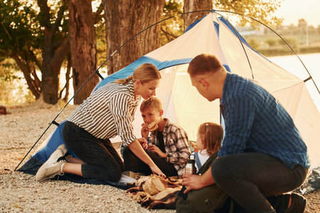 Sitting on the ground. Family of mother, father and kids is on the campingの写真素材
