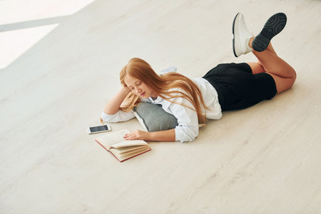 Reading book. Female teenager with blonde hair is at home at daytimeの写真素材