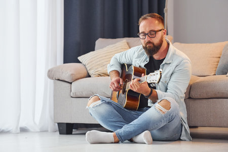 Creative occupation. Man in casual clothes and with acoustic guitar is indoorsの写真素材