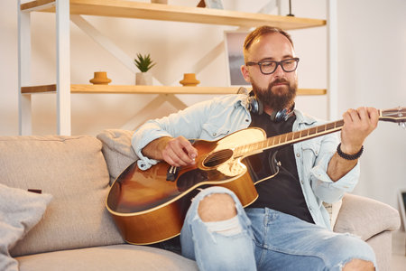 Creative occupation. Man in casual clothes and with acoustic guitar is indoorsの写真素材