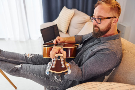 Having good time practicing. Man in casual clothes and with acoustic guitar is indoorsの写真素材
