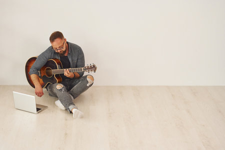With laptop. Man in casual clothes and with acoustic guitar is indoorsの写真素材