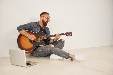 With laptop. Man in casual clothes and with acoustic guitar is indoorsの写真素材