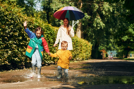 Front view. Mother with her little son and daughter have a walk outdoors in the park after the rainの写真素材