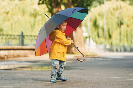 Little boy in yellow coat have a walk outdoors in the park after the rainの写真素材