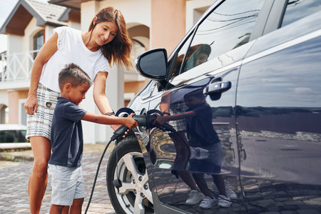 Charging the car. Woman with little boy near the the modern automobile at daytimeの写真素材