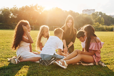 With woman. Group of happy kids is outdoors on the sportive field at daytimeの写真素材