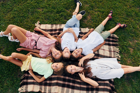 Having a rest and laying down. Group of happy kids is outdoors on the sportive field at daytimeの写真素材