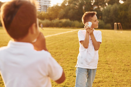 Two boys having fun by using tin can telephone on the sportive fieldの写真素材