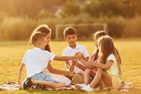 Communicating with each other. Group of happy kids is outdoors on the sportive field at daytimeの写真素材