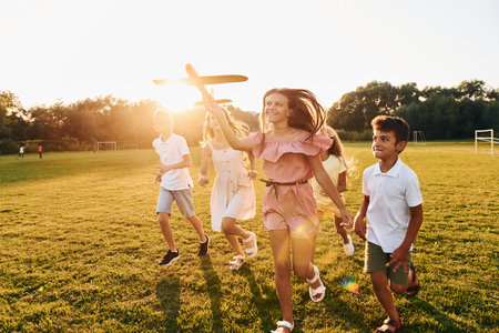 Playing with toy plane. Group of happy kids is outdoors on the sportive field at daytimeの写真素材