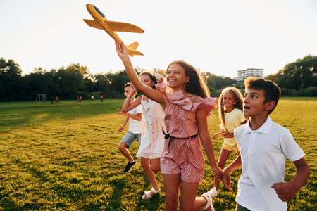 Playing with toy plane. Group of happy kids is outdoors on the sportive field at daytimeの写真素材