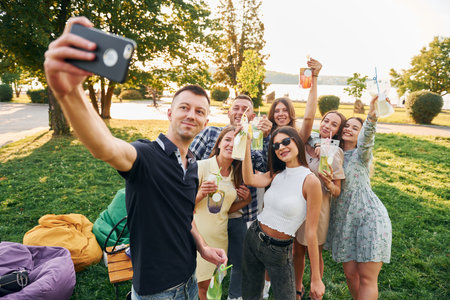 Man taking a selfie. Group of young people have a party in the park at summer daytimeの写真素材