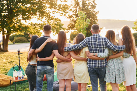 View from behind. Group of young people have a party in the park at summer daytimeの写真素材
