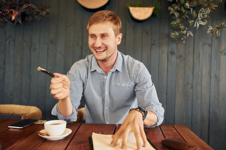 With cup of tea. Adult man is sitting indoors by the table in the cafeの写真素材