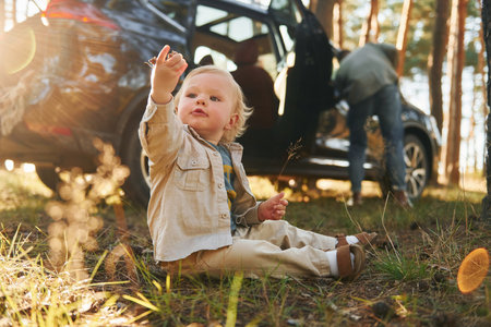 Girl is sitting on the ground. Happy family of father, mother and little daughter is in the forestの写真素材
