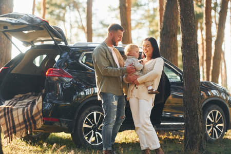 Woman holding girl. Happy family of father, mother and little daughter is in the forestの写真素材