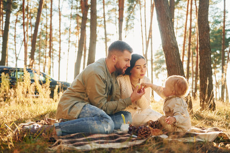 Illuminated by sunlight. Happy family of father, mother and little daughter is in the forestの写真素材