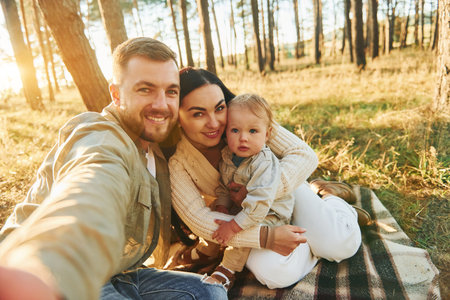 Making a selfie. Happy family of father, mother and little daughter is in the forestの写真素材