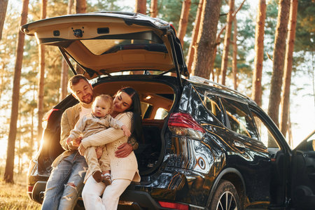 With black colored automobile. Happy family of father, mother and little daughter is in the forestの写真素材