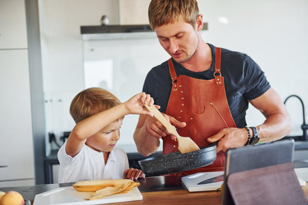 Using tablet to learn how to cook. Father and son is indoors at home togetherの写真素材