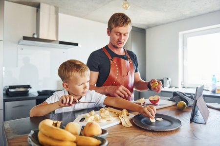 Man is in the apron on kitchen. Father and son is indoors at home togetherの写真素材