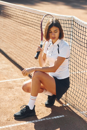 Sitting and posing. Female tennis player is on the court at daytimeの写真素材