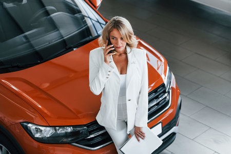 Holding phone. Woman in formal clothes is indoors in the autosalonの写真素材