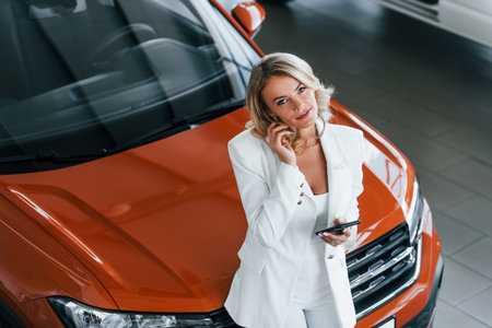 Leaning on the car. Woman in formal clothes is indoors in the autosalonの写真素材